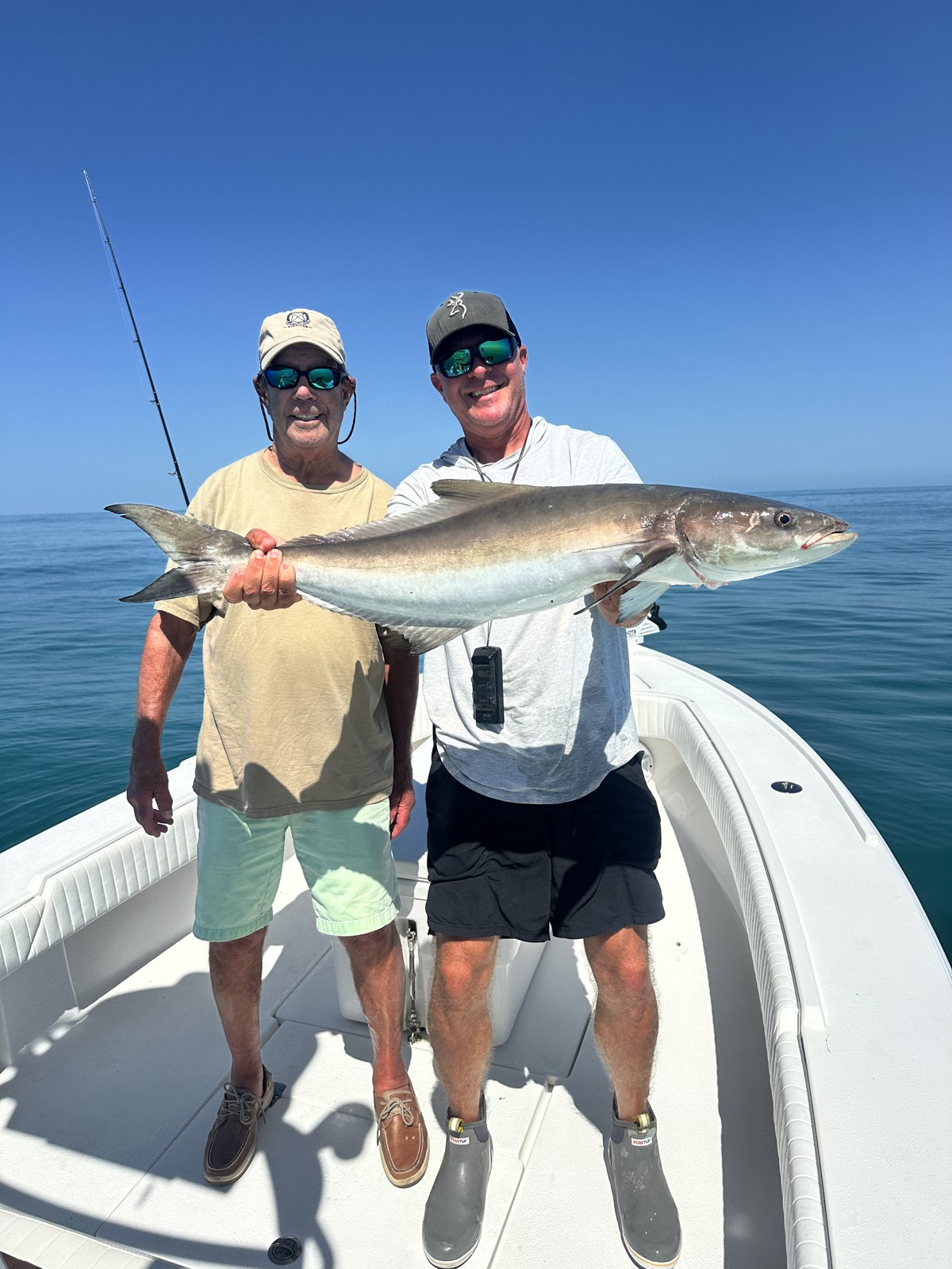 Two anglers holding a cobia on flat calm Gulf water