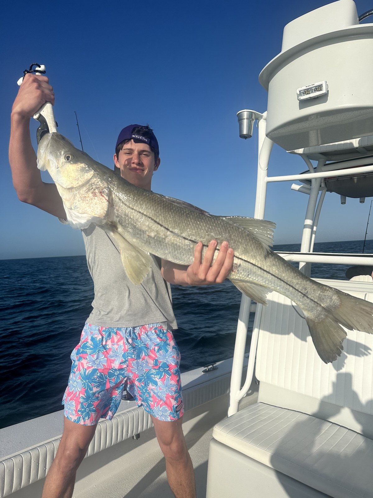 Young angler hoisting a long snook under blue skies
