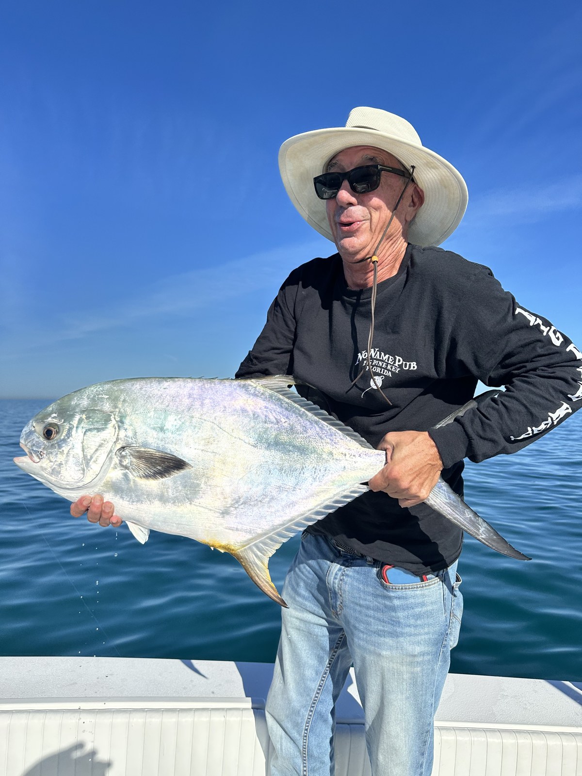 Angler in a straw hat holding a bright silver permit